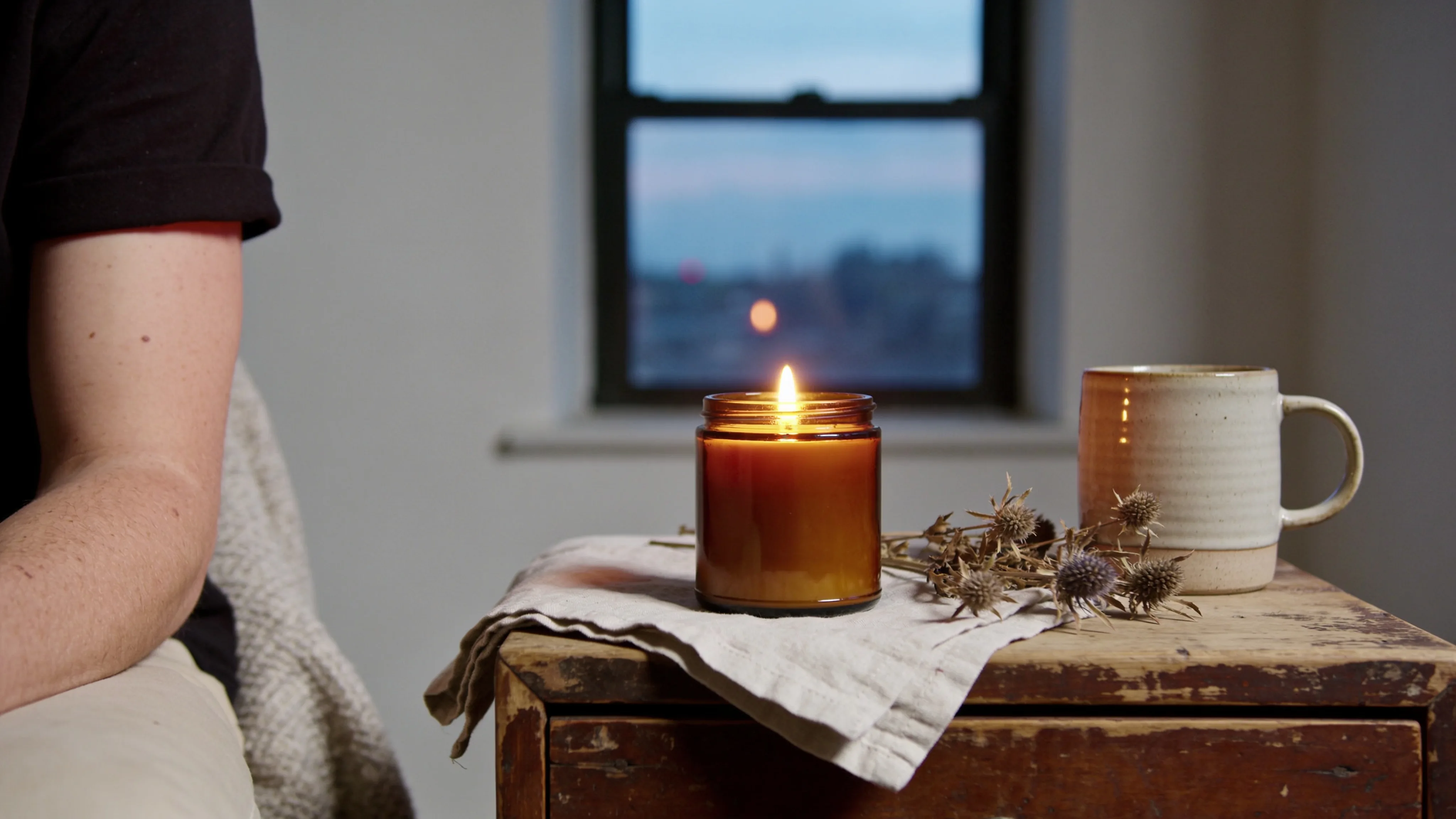 Lit Cedarwood and Amber soy candle glowing warmly on a wooden shelf